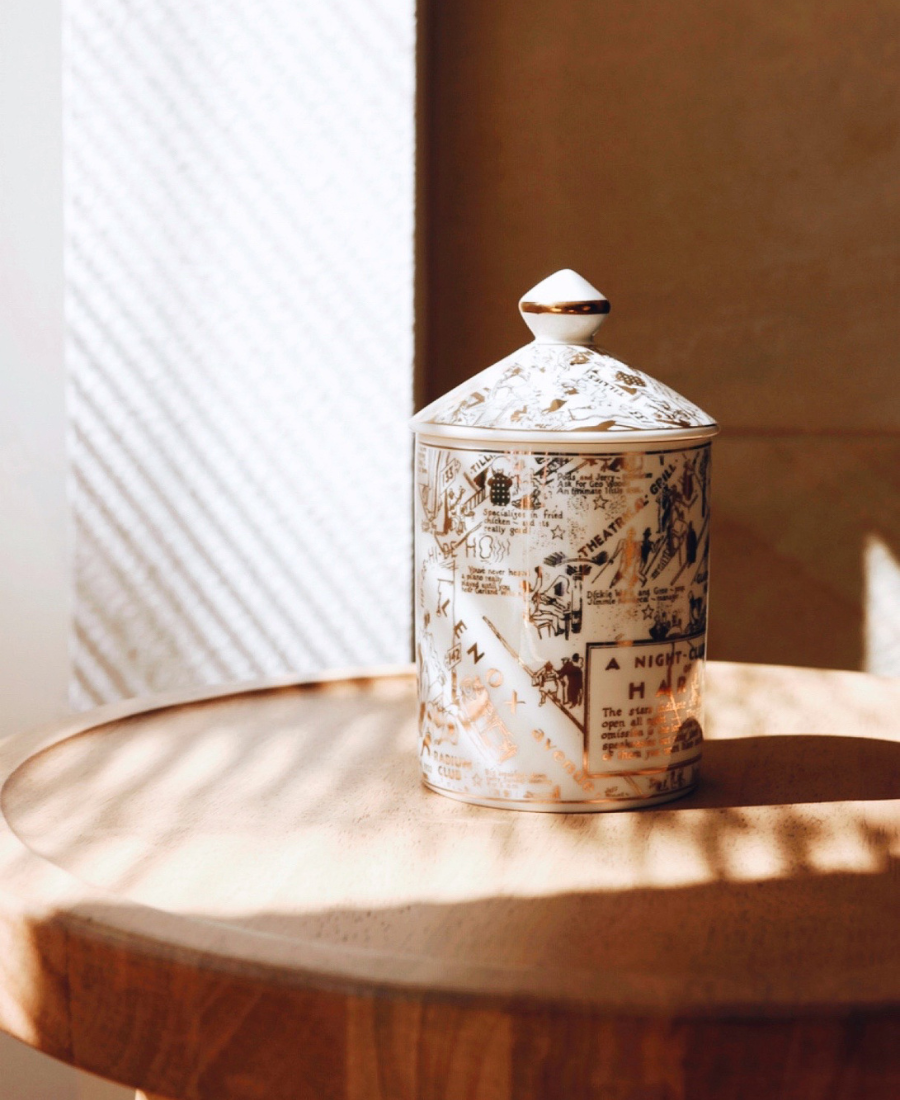 Speakeasy Ceramic Candle topped with lid on a wooden table lit through window blinds.