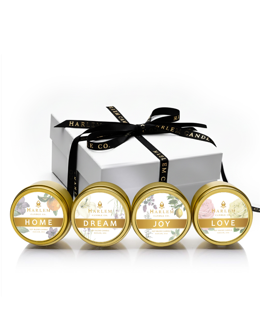 Set of four small containers with lids labeled 'Home', 'Dream', 'Joy', and 'Love' in front of a white box with a black ribbon.