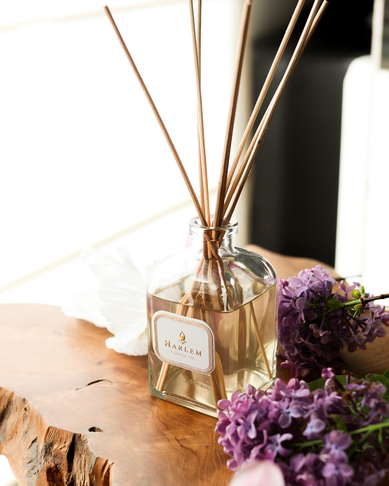 This is a vertical image of the clear glass "Joy" Botanical Diffuser bottle with colorful flowers in the background.
