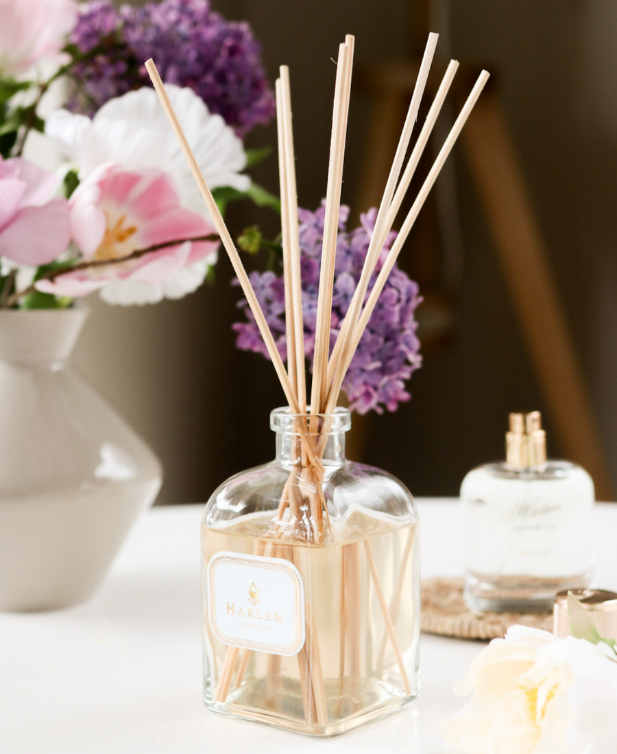 Joy Reed Diffuser on a white table with flowers and the Billie Perfume.