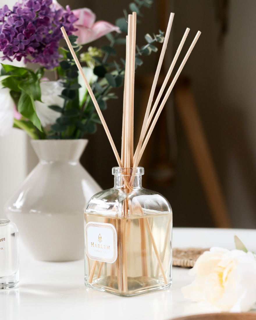 Bloom Reed Diffuser on a white table with flowers.