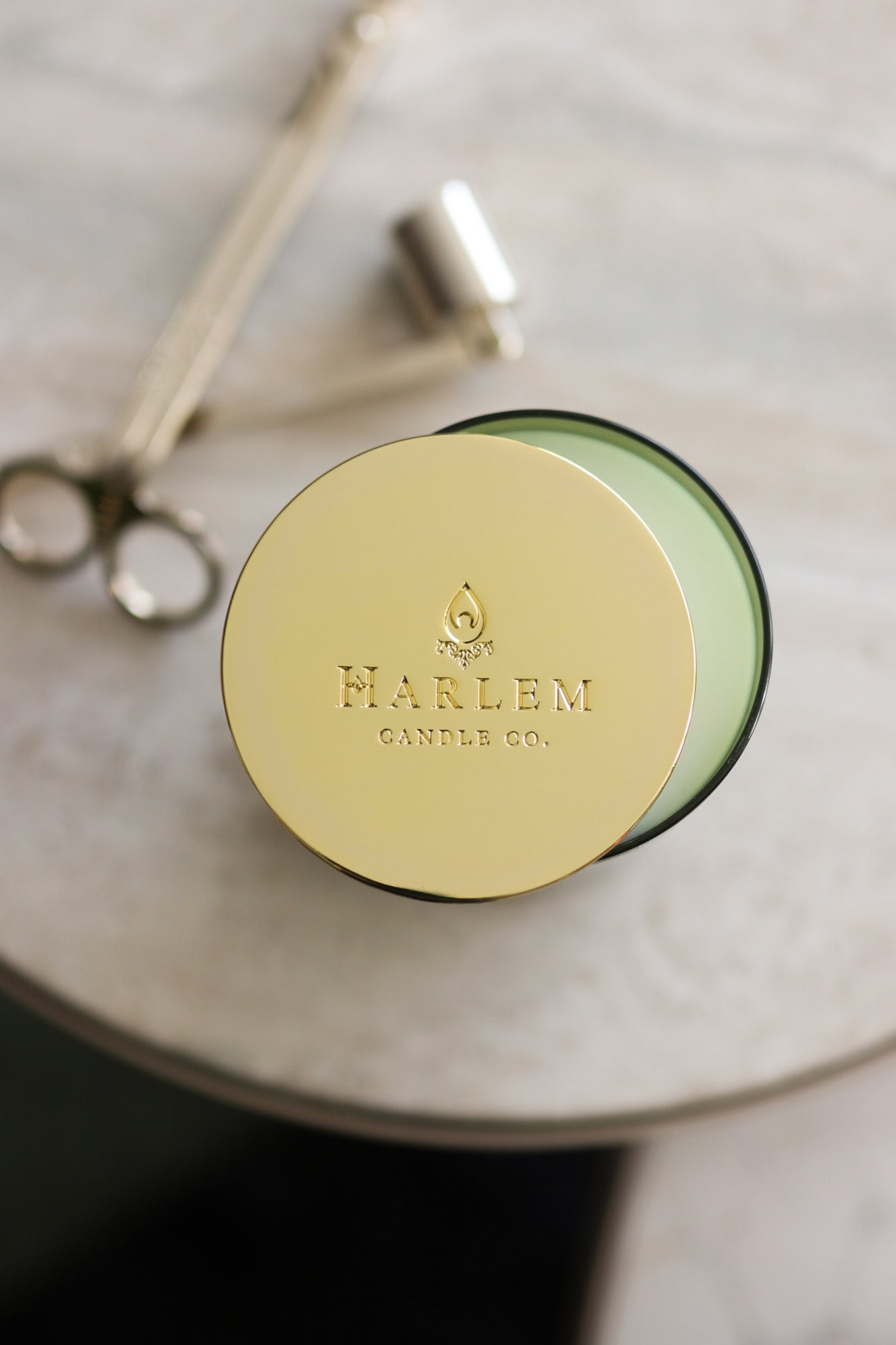 This is a lifestyle image of our gold candle lid on our holiday candle pictured next to the wick trimmer and snuffer set.