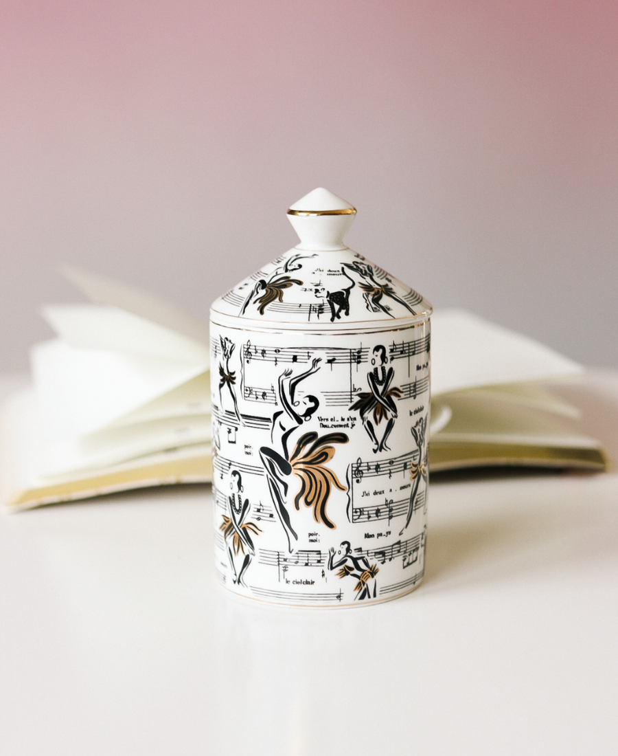 Deux Amours Ceramic Candle on a white table with a book and ombre purple background.