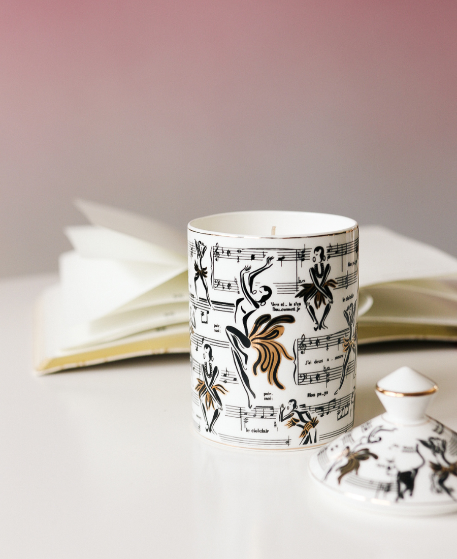 Deux Amours Ceramic Candle on a white table next to a book and lid and ombre purple background.