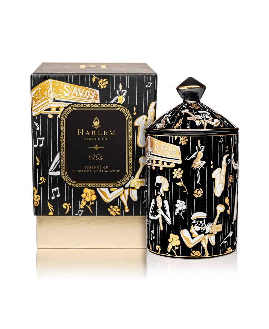 This is an image of our black gold and white Duke, ceramic candle with a lid. It features illustrations of Billie Holiday, the savoy ballroom, Duke Ellington, and other original illustrations. This candle is featured next to its decorative box.
