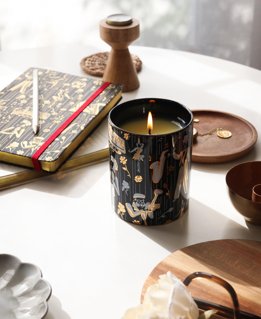 Duke Ceramic Candle on a white table with wooden trays, jewelry, and journals.