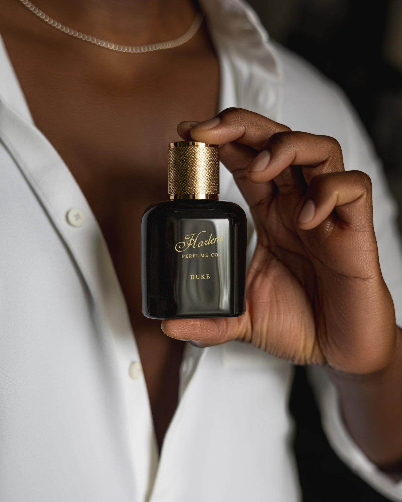 This is an image of our Duke perfume being held by one hand of a make model, wearing a white button down shirt
