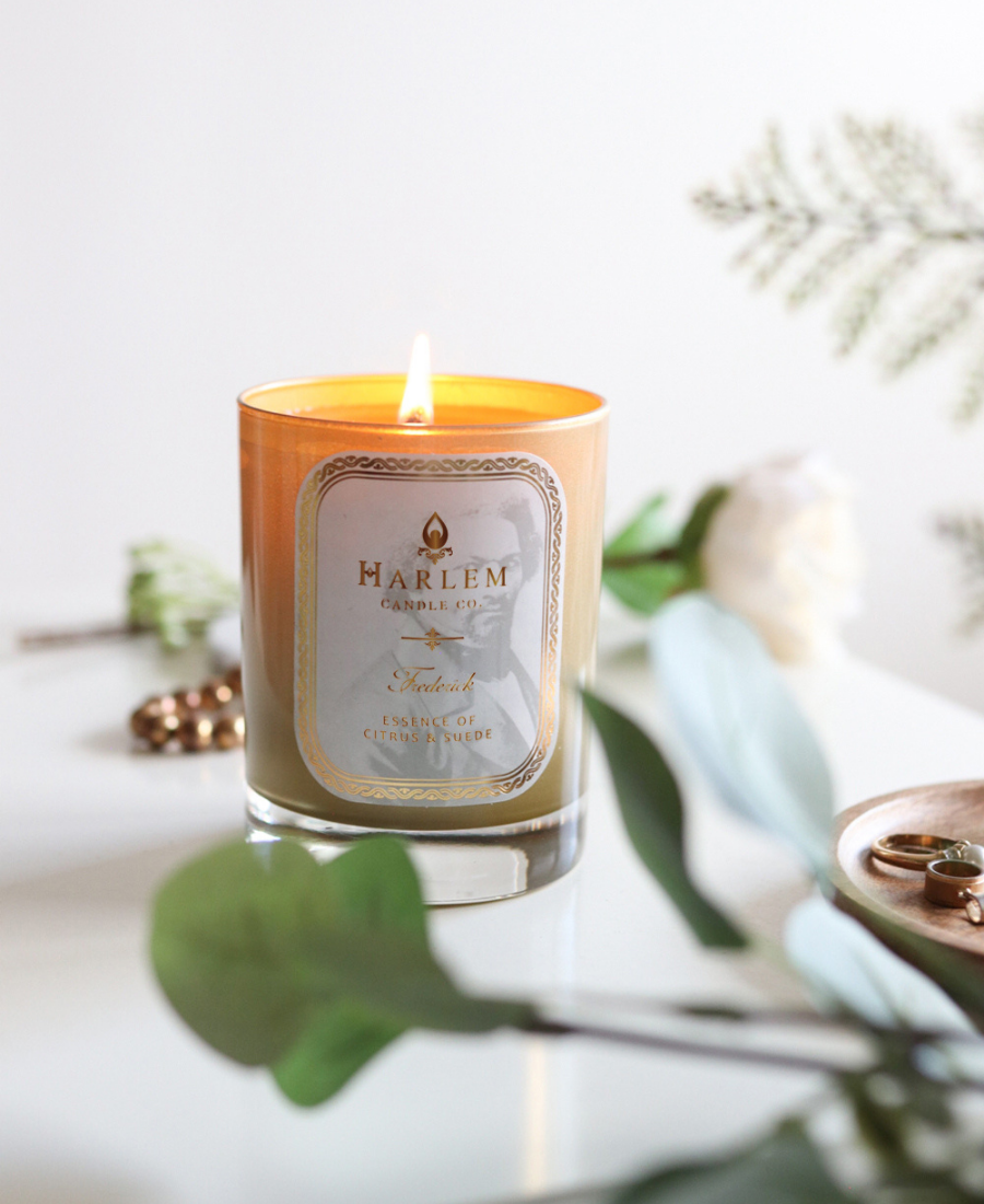 Frederick Candle on a white table with jewelry and greenery.