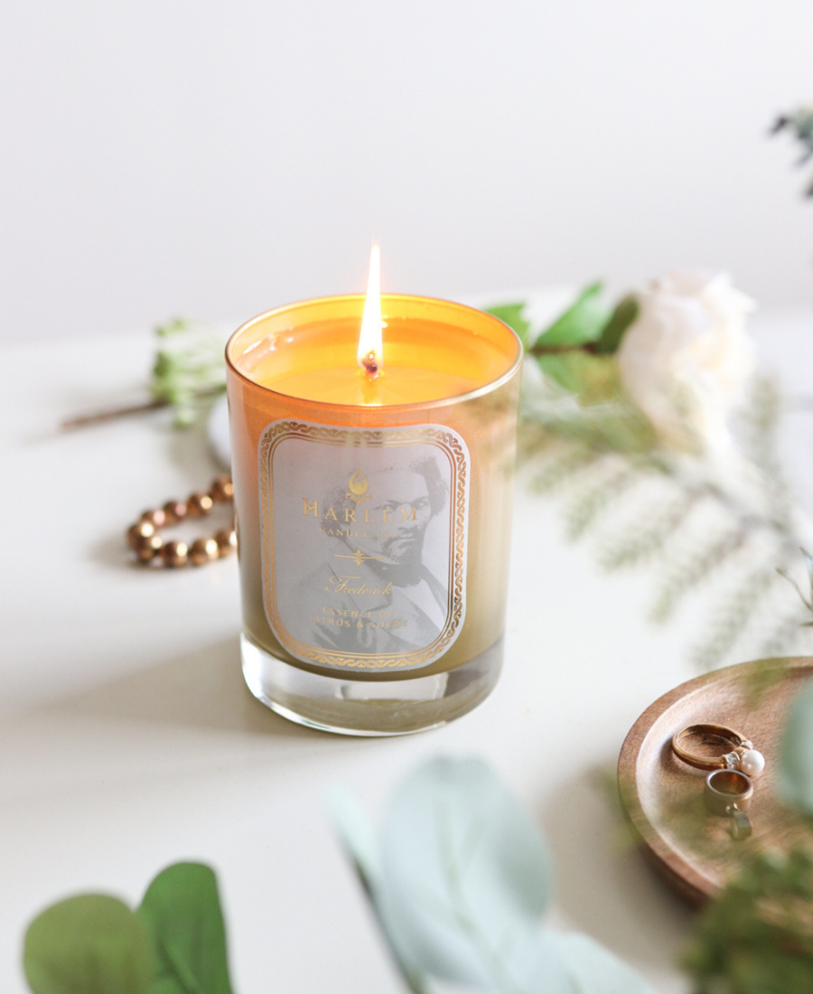 Frederick Candle on a white table with jewelry and greenery.