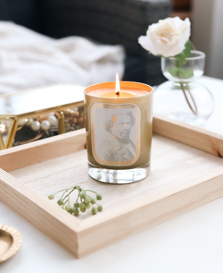 Frederick Candle on a wooden tray with jewelry and greenery.