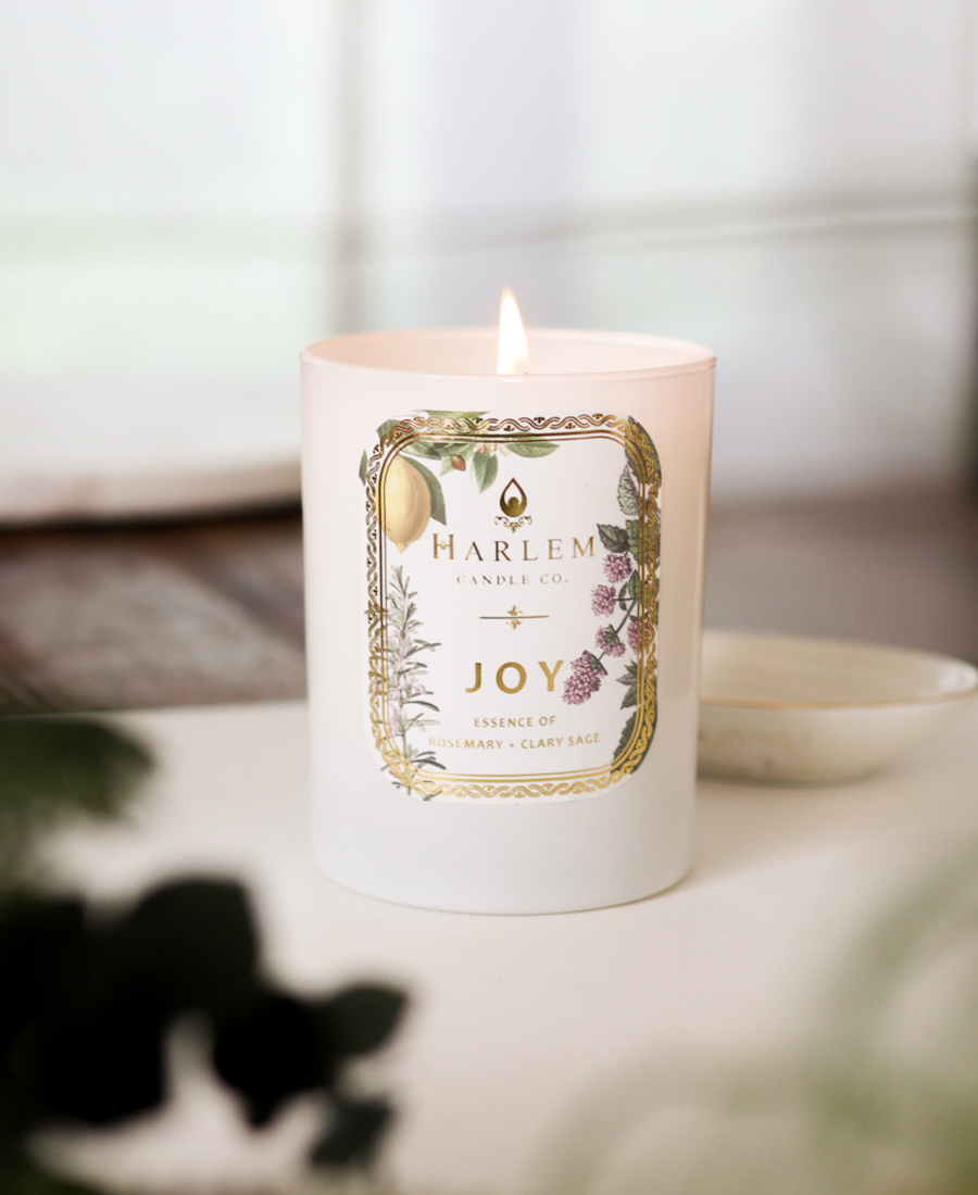 Joy Candle on a white table with a white ceramic dish and greenery.