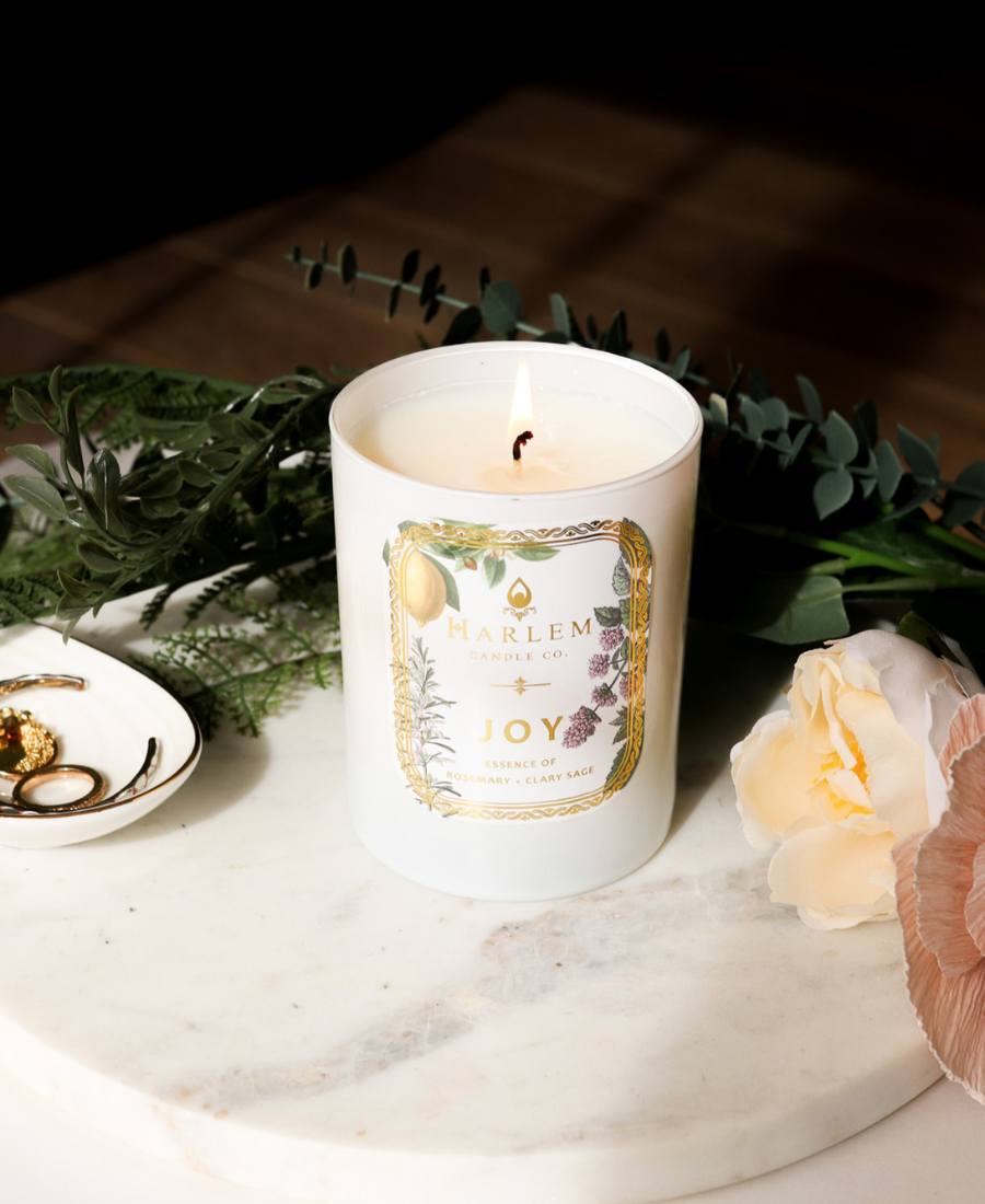 Joy Candle on a white marble tray with jewelry, flowers, and greenery.