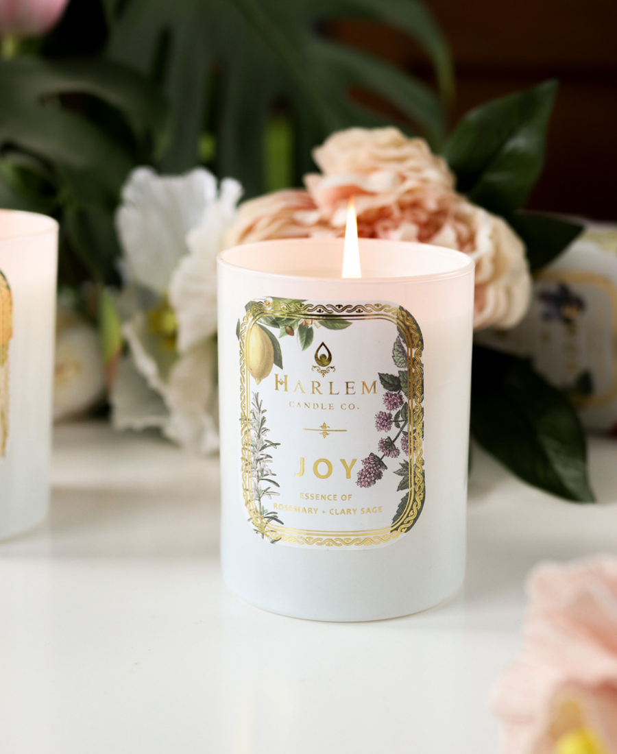 Joy Candle on a white table with flowers and greenery.