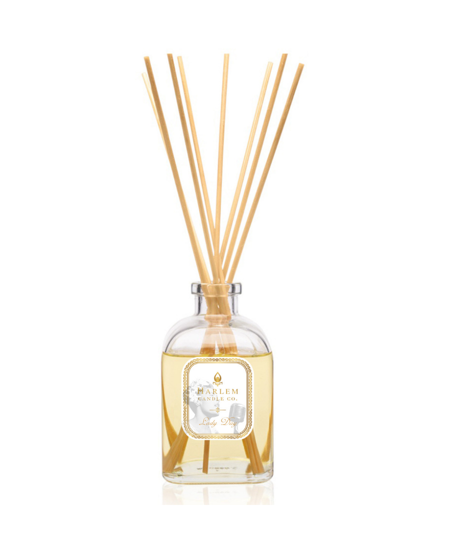 Lady Day reed diffuser bottle filled with pale golden liquid with multiple natural wood reed sticks rising above the top, set against a plain white background.