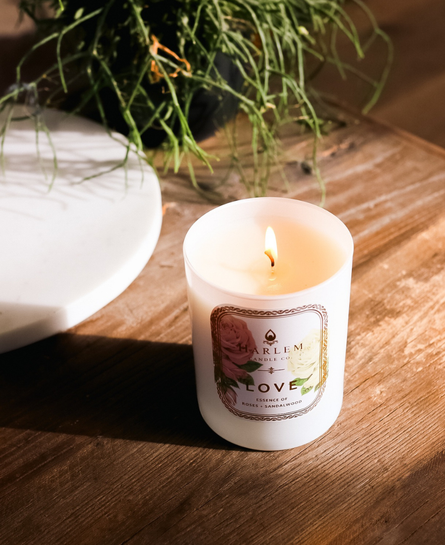 Love Candle on a wooden table with a white tray and greenery.