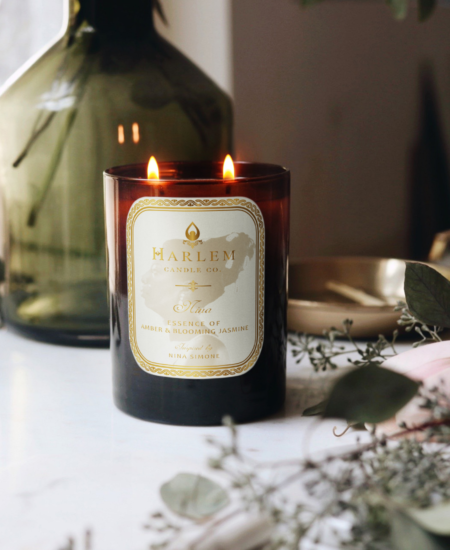 Nina Candle on a white table with greenery, a gold tray, and a green vase.