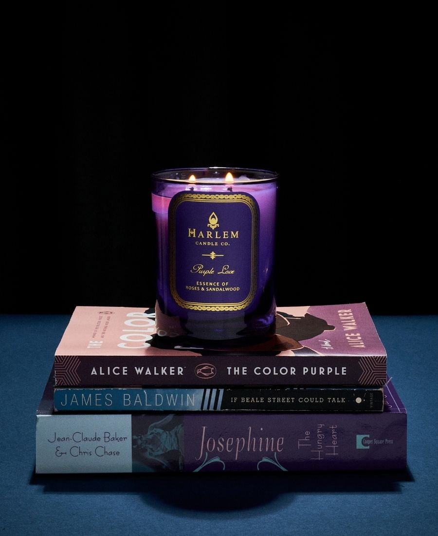 Purple Love candle on a stack of books with a black background.