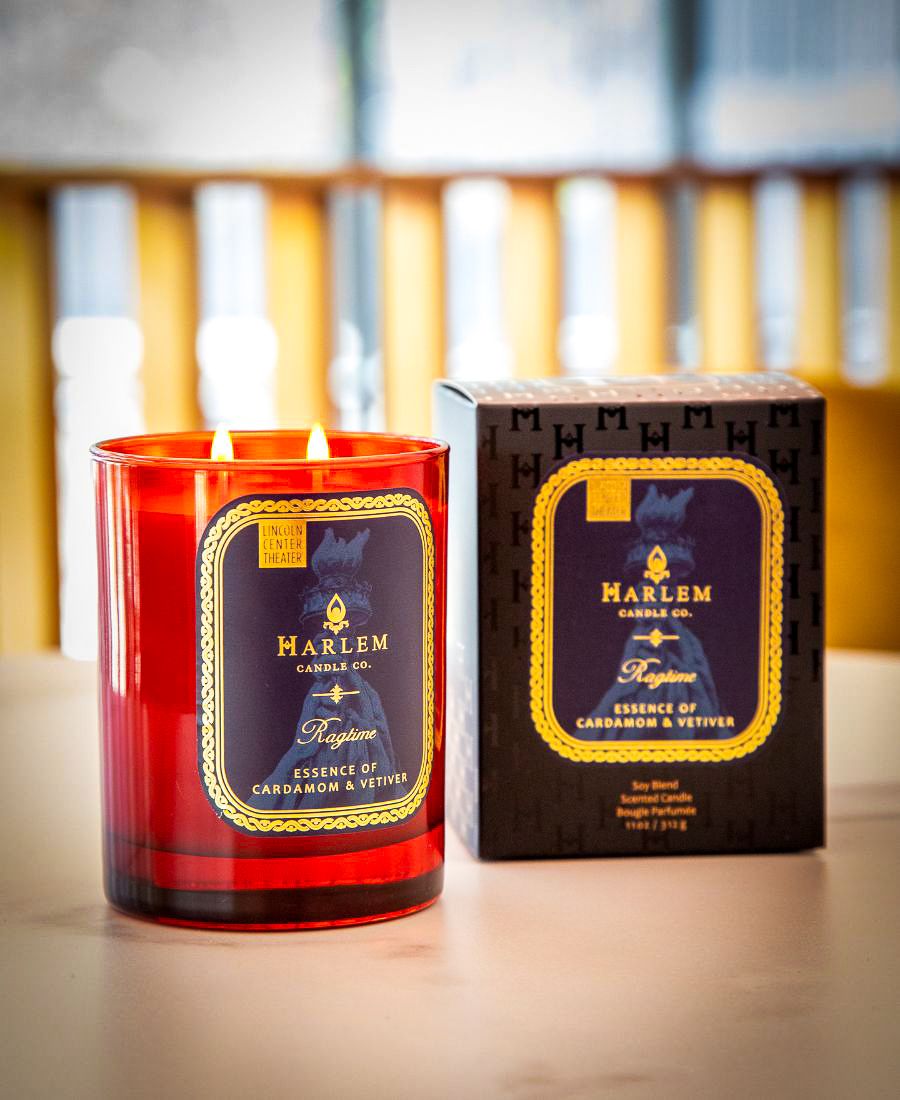 Harlem Candle Co. candle with red glass and black label on a wooden surface.