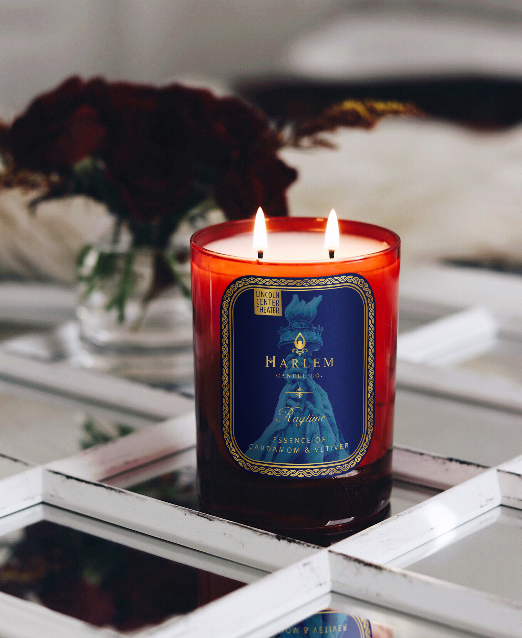 Harlem Candle Co. Ragtime candle with a blue label in a red glass on a reflective surface.