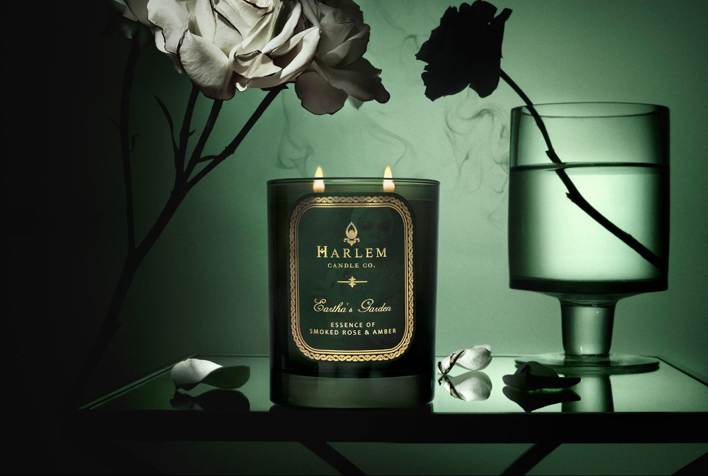 Harlem Candle Co. candle with flowers and a glass on a dark surface