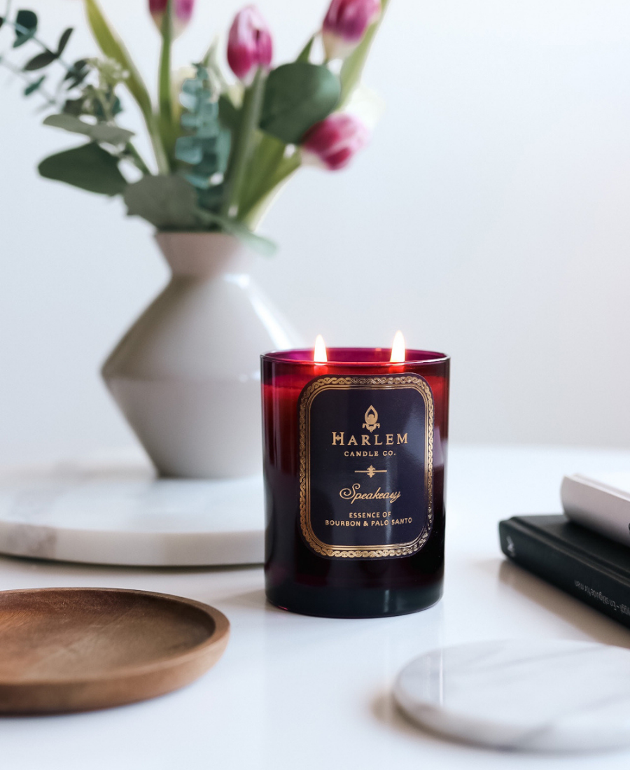Speakeasy Candle on a white table with wood and marble trays and flowers.