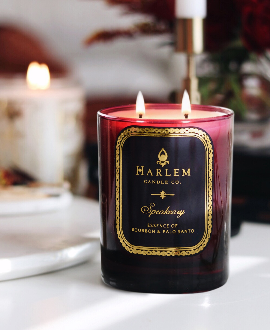 Speakeasy Candle on a white table with flowers and candles in the background.