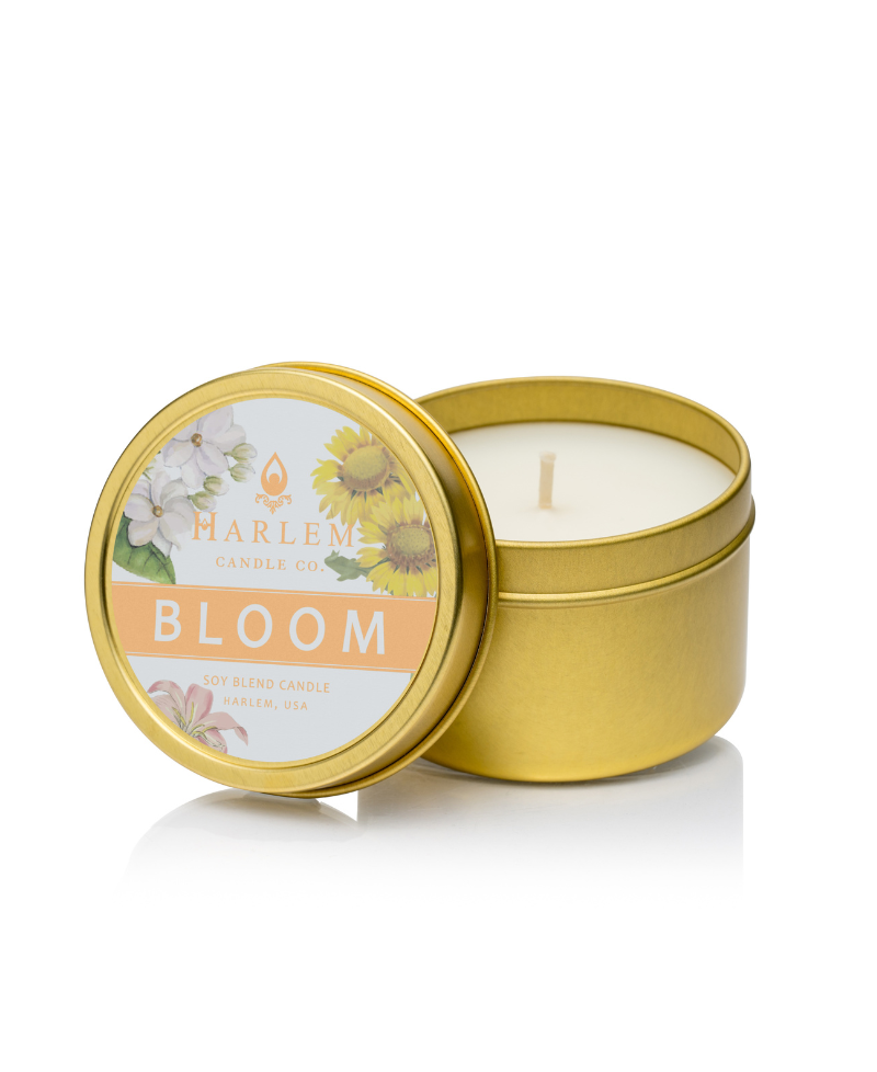 Picture of the Bloom Travel candle. It is in a gold tin with a white label with flowers on the top.