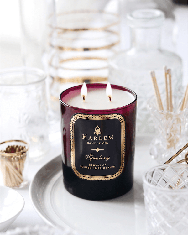 This is a lifestyle image of our Speakeasy candle in a burgundy glass surrounded by crystal bottles.