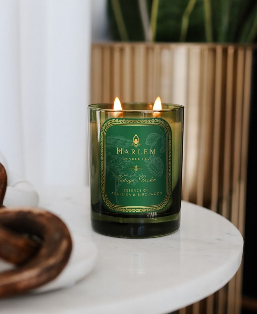 Vintage Garden Candle on a white table with a potted plant in the background.