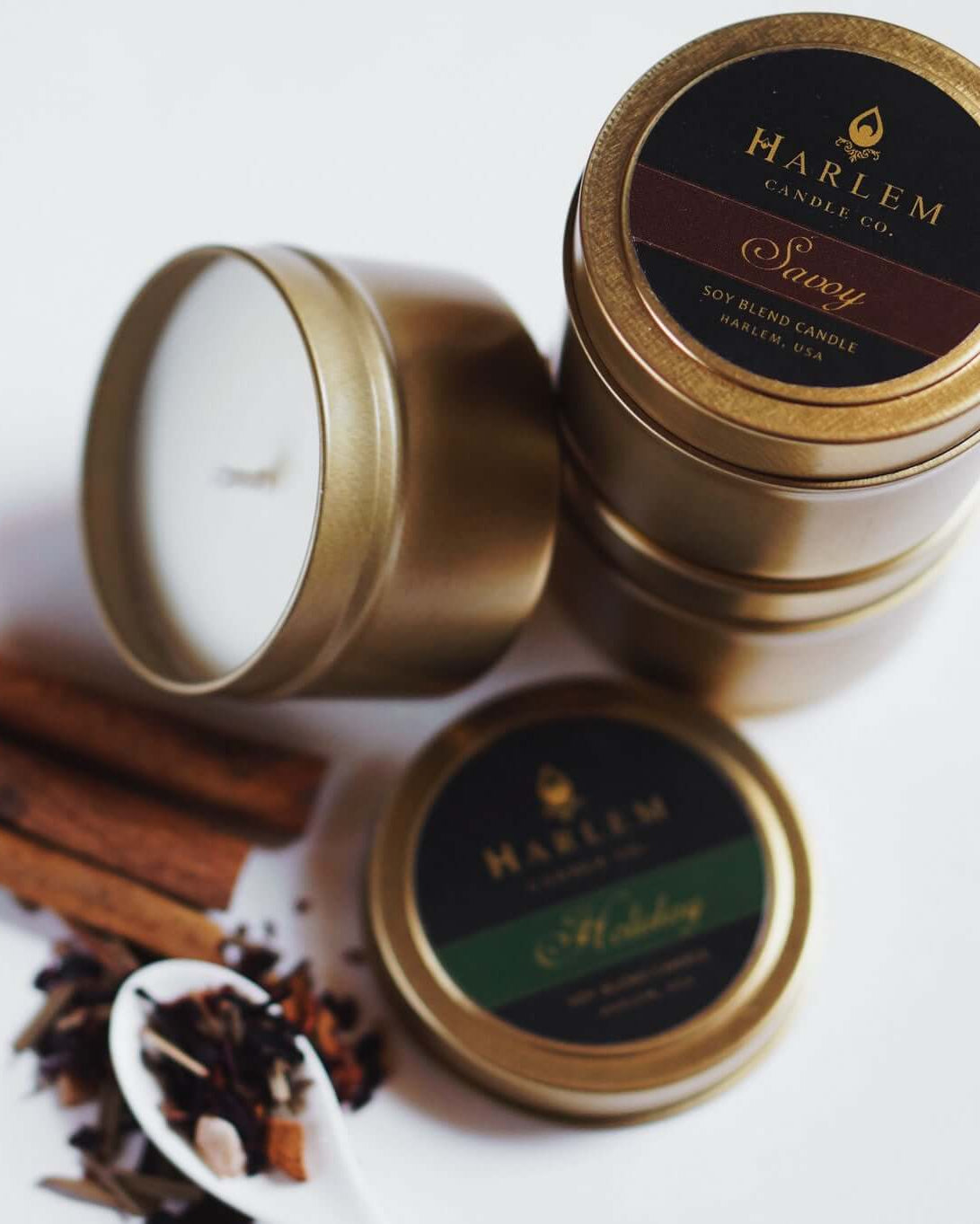 Our Savoy travel tin candle sitting on top of other travel tins displayed beautiful with cinnamon sticks on a white table.