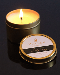Gorgeous lifestyle image of our softly burning 1 wick Lady Day 4 oz travel candle on top of a black background.