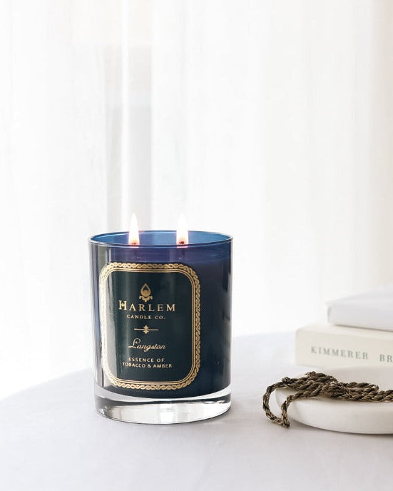 Our 4 fluid oz Langston Reed Diffuser with blue glass and reeds placed in diffuser glass sitting on a white table next to a 11oz Langston Candle.