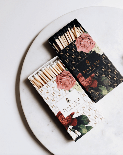 This is a gorgeous lifestyle image of two of our match boxes, our white floral art deco pattern and our black floral art deco pattern, sitting on top of a white porcelain plate with a white background.
