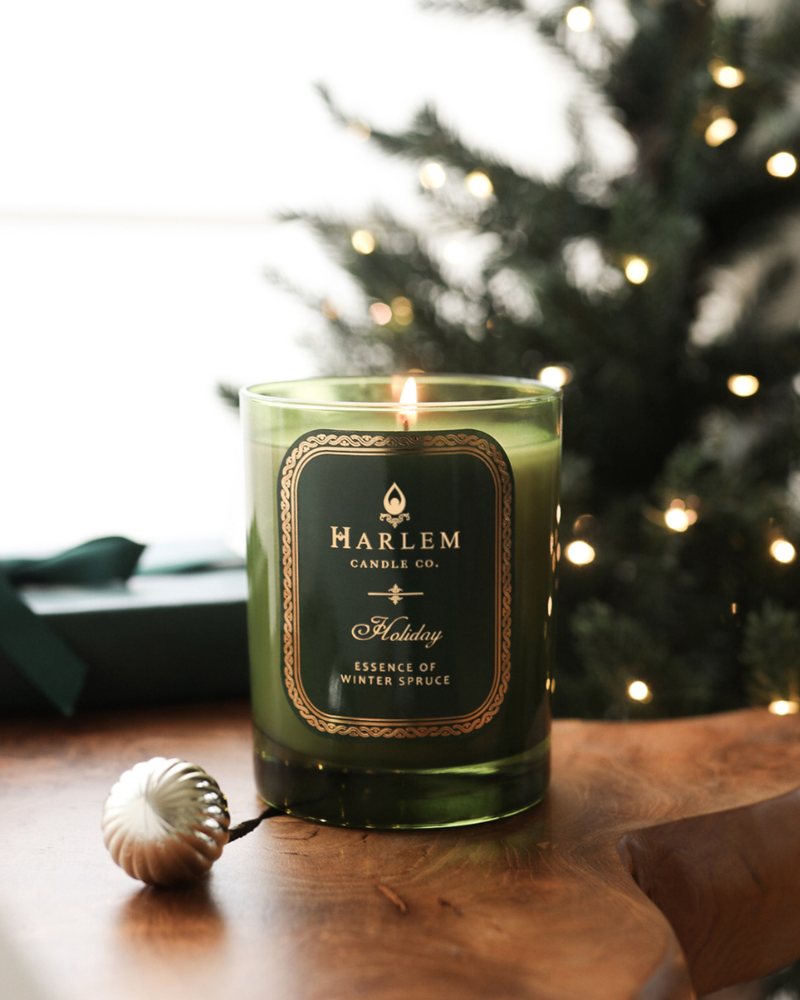 Harlem Candle Co. candle on a wooden surface with a blurred Christmas tree in the background