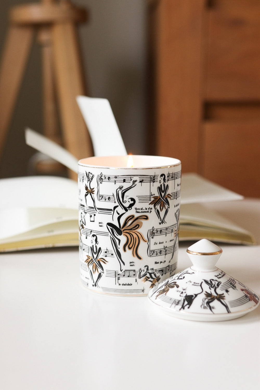 This is a lifestyle image of our Deux Amours ceramic candle illuminated. The design on the vessel features our original illustrations of Josephine Baker and the Deux Amours sheet music where she would hide her spy secrets when she was touring and performing while working as an anti-Nazi spy.