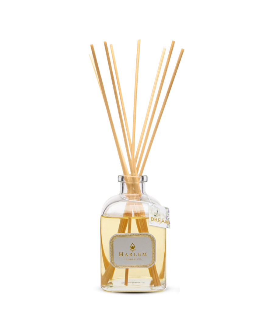 Dream reed diffuser bottle with tag and multiple natural wood reed sticks rising above the top, set against a plain white background.