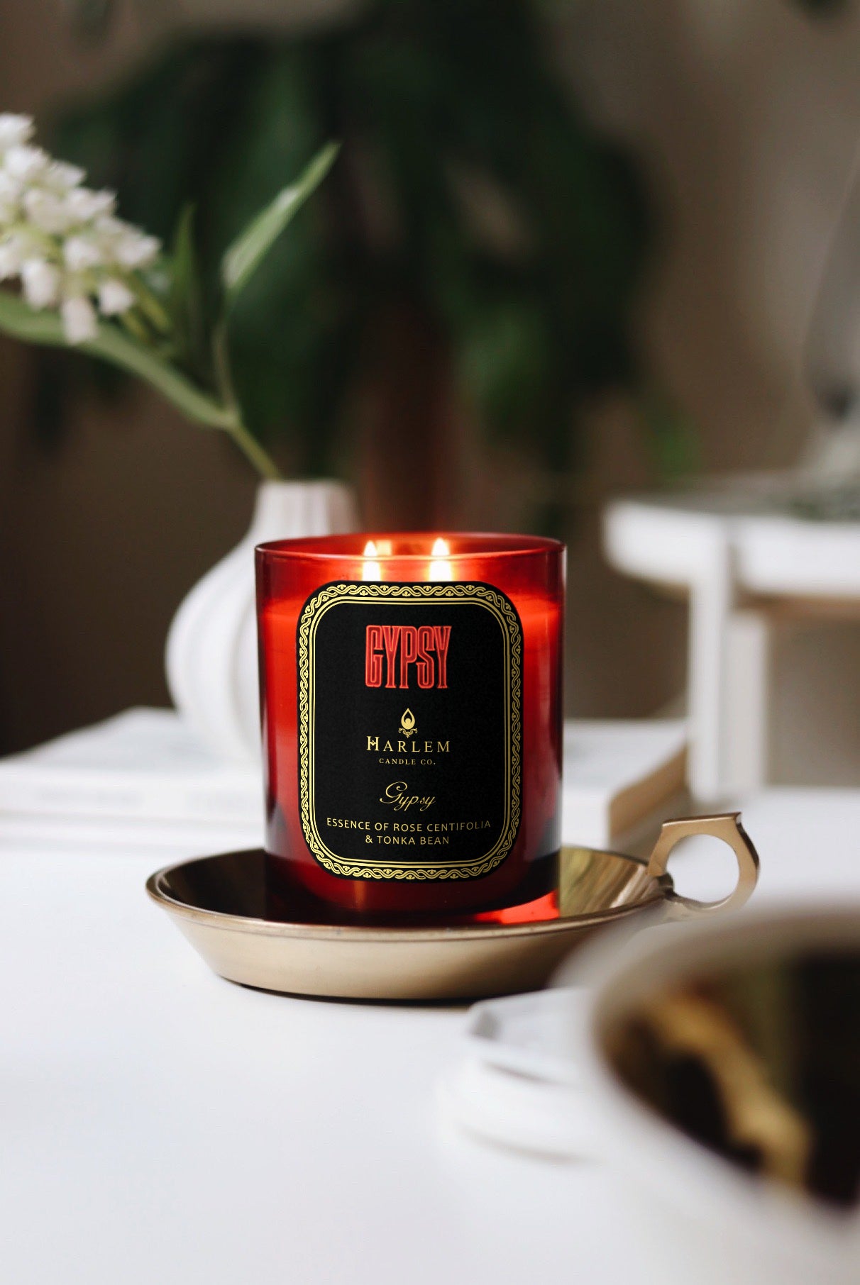 This is a vertical image of our gypsy candle and a lifestyle setting with a white flower and greenery in the background.