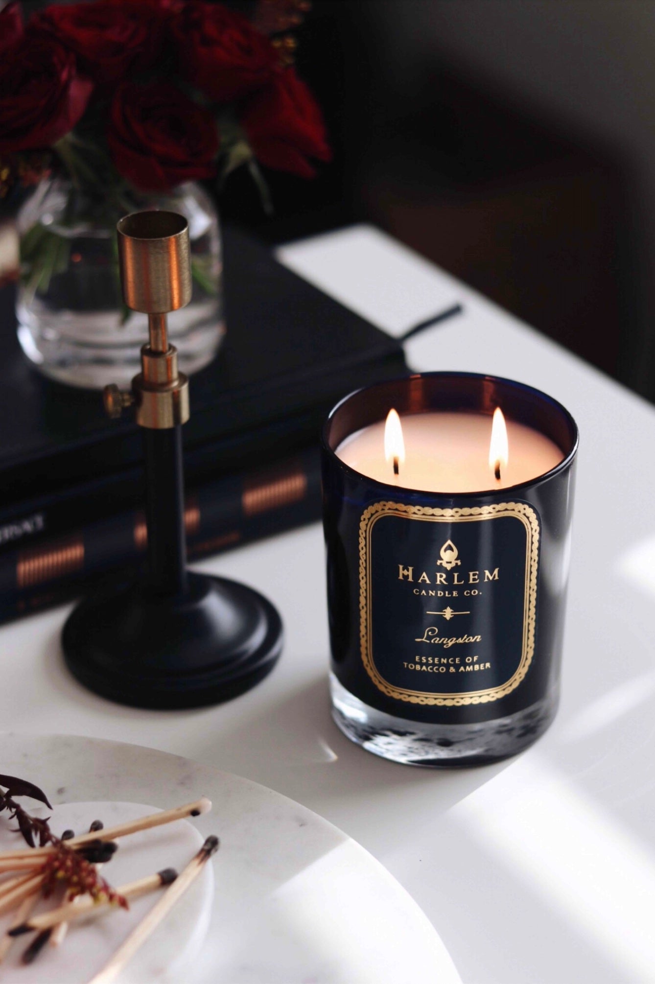 This is an image of our Langston candle illuminated next to used to matches, pretty red roses, and an empty candle holder.
