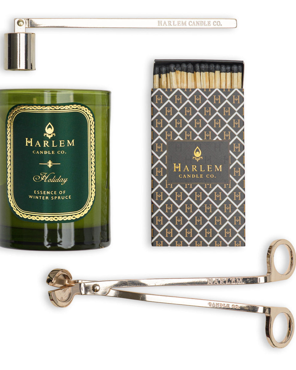 This is an image of our holiday candle featured next to the snuffer, trimmer and a set of matches in an art deco style match box.