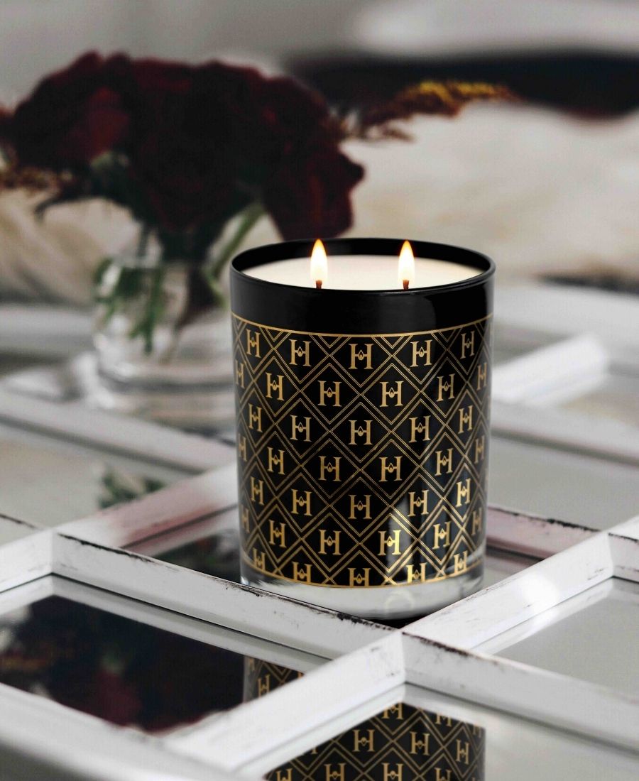 Candle with a black and gold pattern on a reflective surface with blurred background