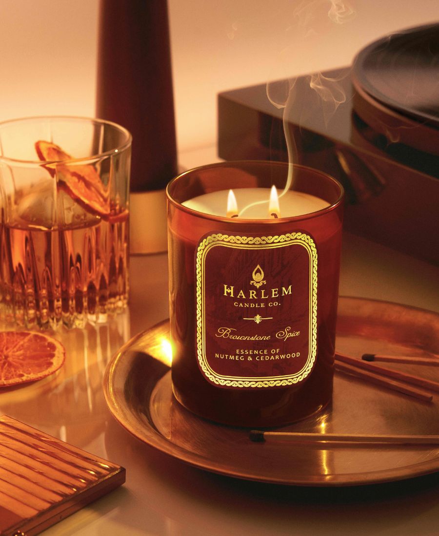 This is an image of the Brownstone Spice Candle in an amber colored with the wicks lit with a little bit of smoke.