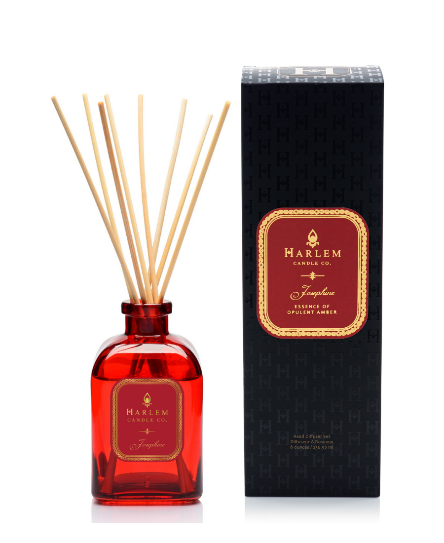 Josephine reed diffuser bottle with natural reeds next to its black textured packaging box on a white background.