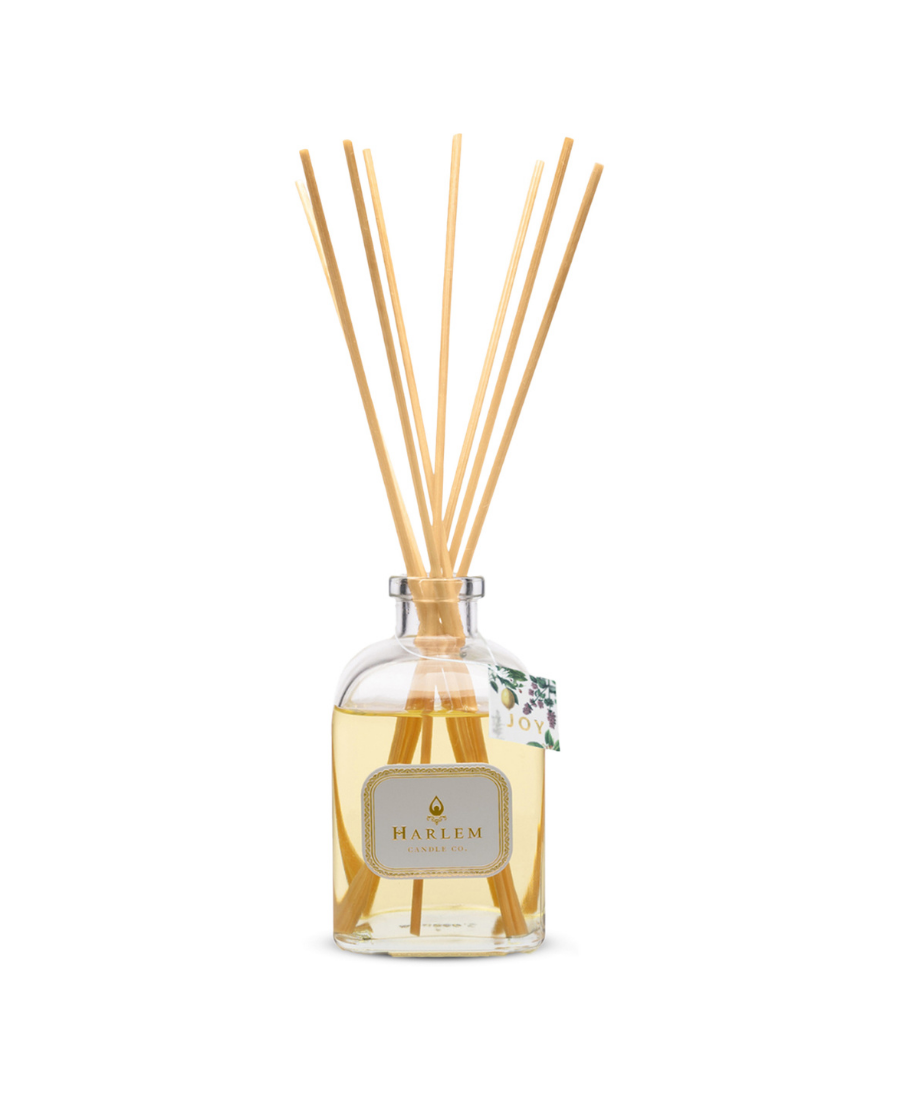 Joy reed diffuser bottle with tag and multiple natural wood reed sticks rising above the top, set against a plain white background.