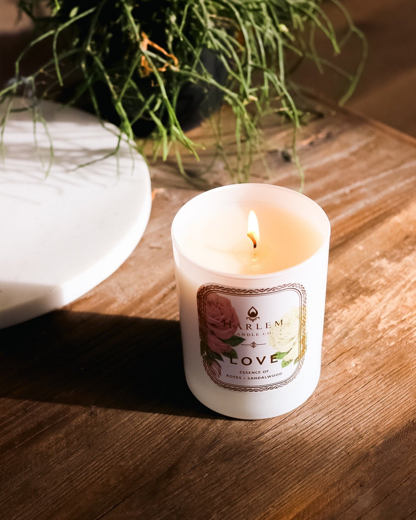 This is an image of the "Love" Luxury Candle on a wooden table with greenery in the background.