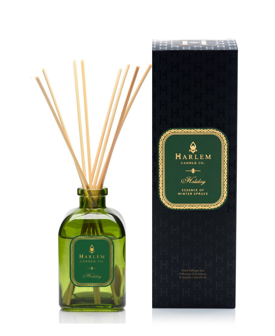 Holiday reed diffuser bottle with natural reeds next to its black textured packaging box on a white background.