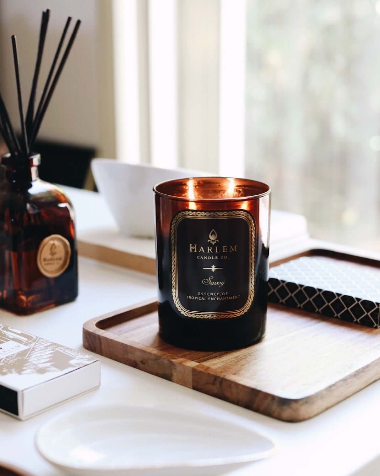 This is a lifestyle image of the lit 11 oz 2 wick Savoy Candle sitting on a wooden tray with a Savoy diffuser in the background.