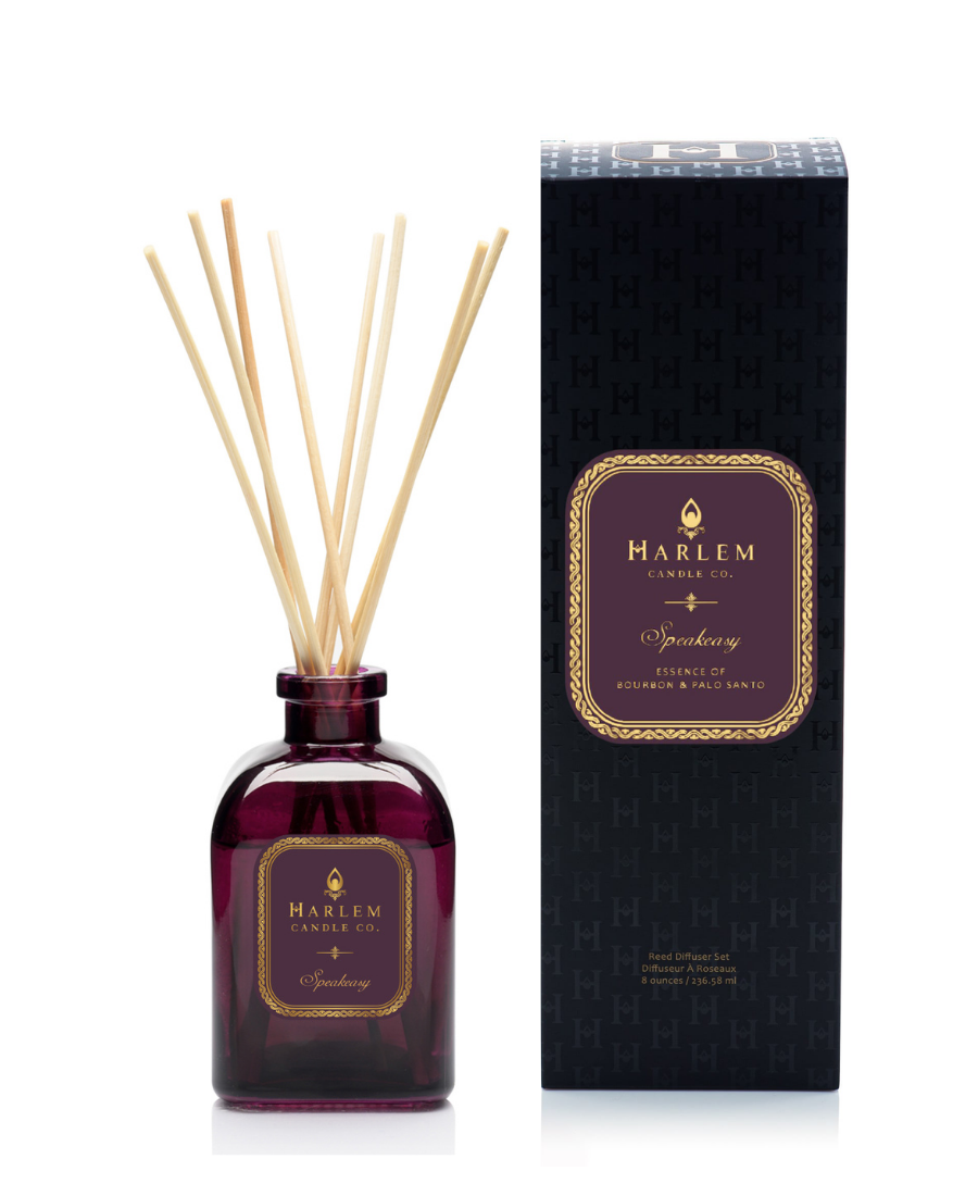 Speakeasy reed diffuser bottle with natural reeds next to its black textured packaging box on a white background.
