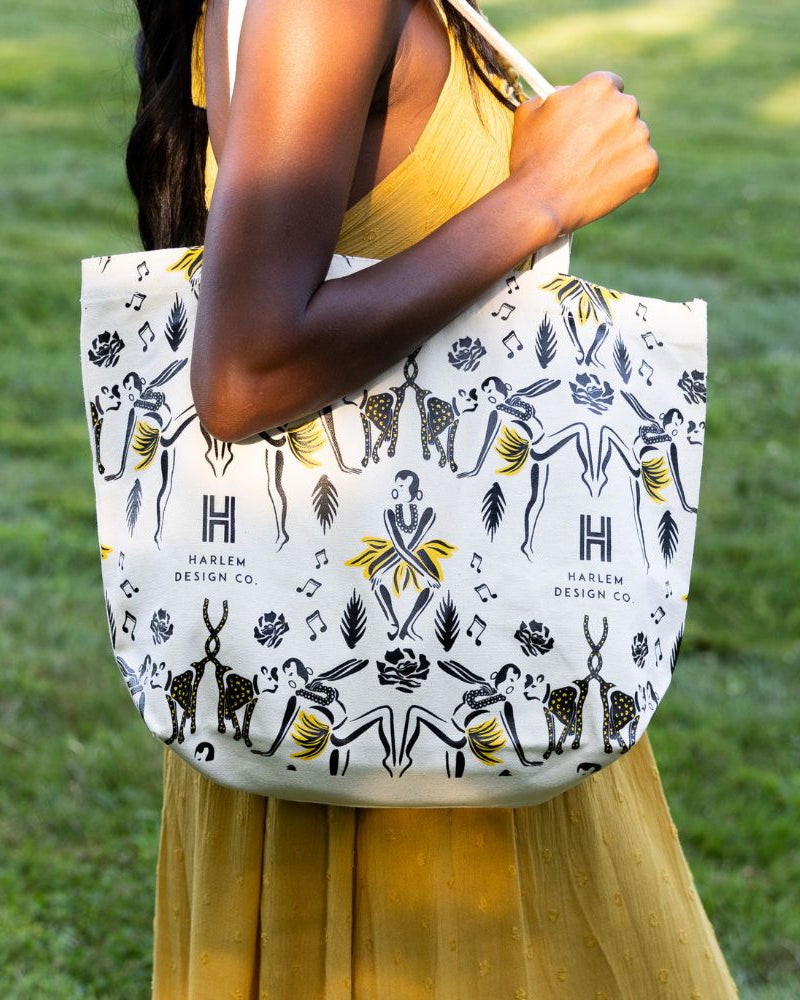 This is an image of our Josephine tote bag featuring illustrations of Josephine Baker and her pet Chiquita.  The bag is being held by a model wearing a yellow dress.
