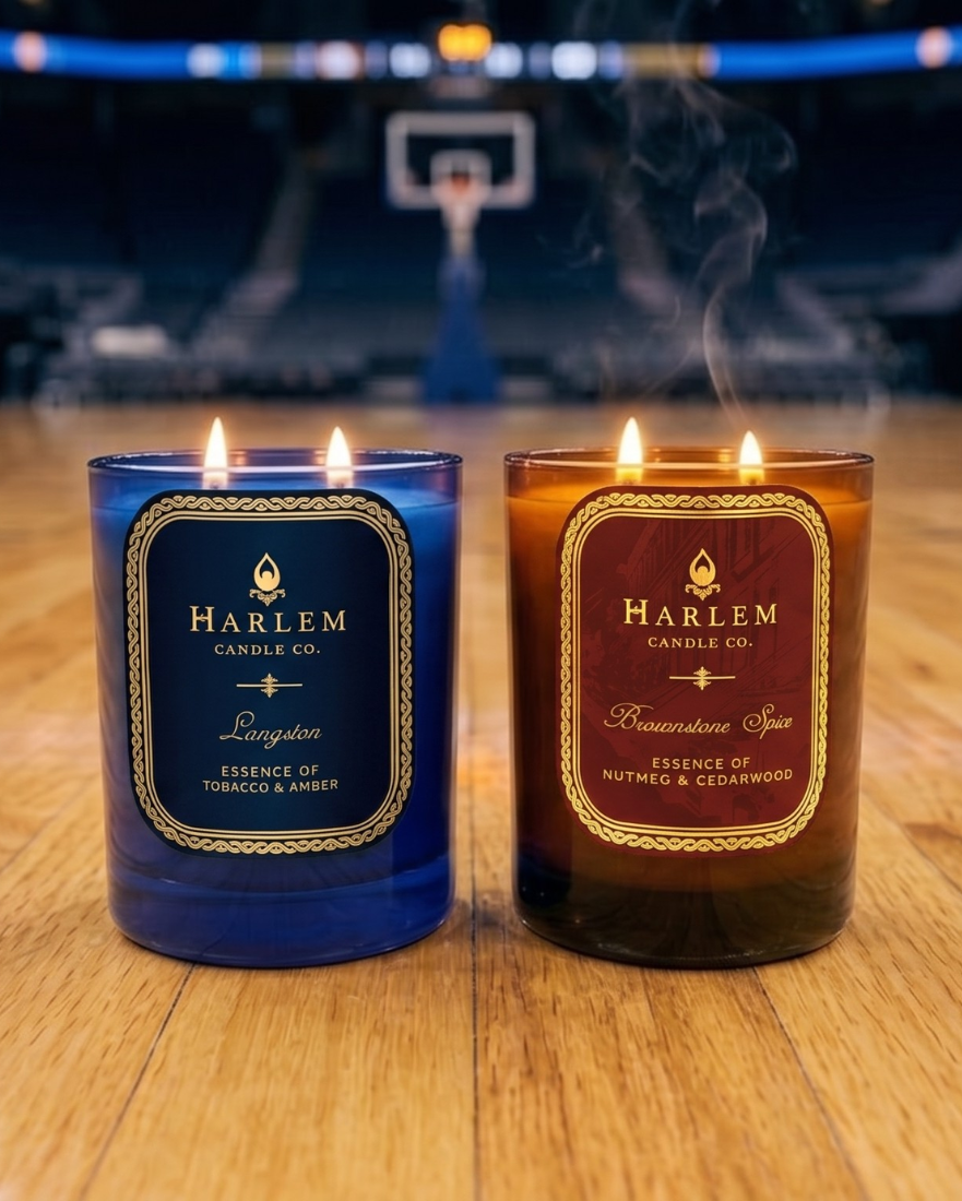 TwoHarlem Candle Co. candles, one blue and one brown, on a wooden surface with a blurred basketball court background.