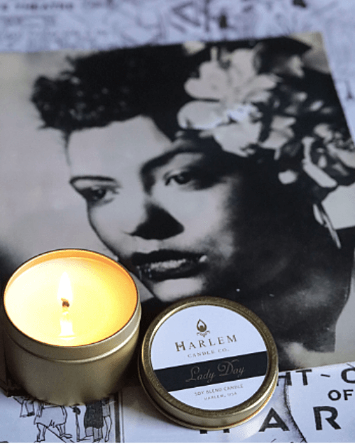 Gorgeous lifestyle image of the lit, 1 wick Lady Day 4 oz travel candle on top of a black and white harlem nights map and a black and white photograph of Billie Holiday.